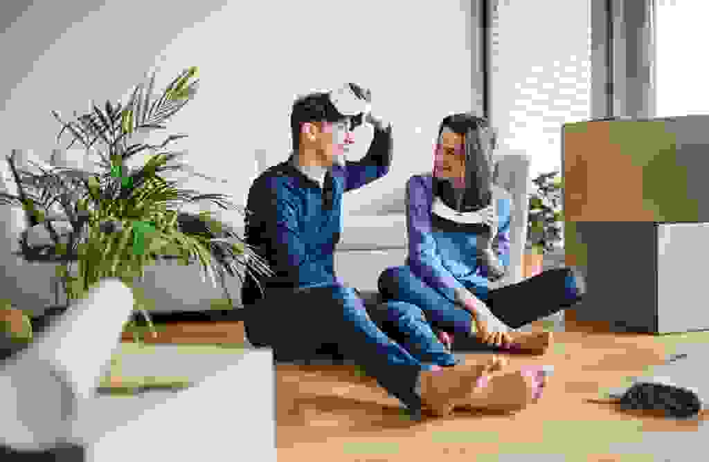 Junges Paar sitzt zwischen Umzugskartons auf dem Fußboden mit VR-Brille